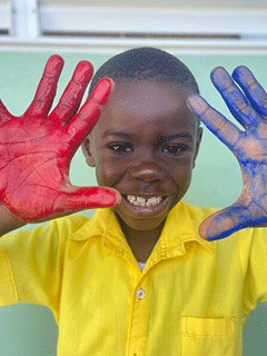 Holistic Haitian Alliance | education elementary image 1 smiling Haitian student with red and blue paint on his hands